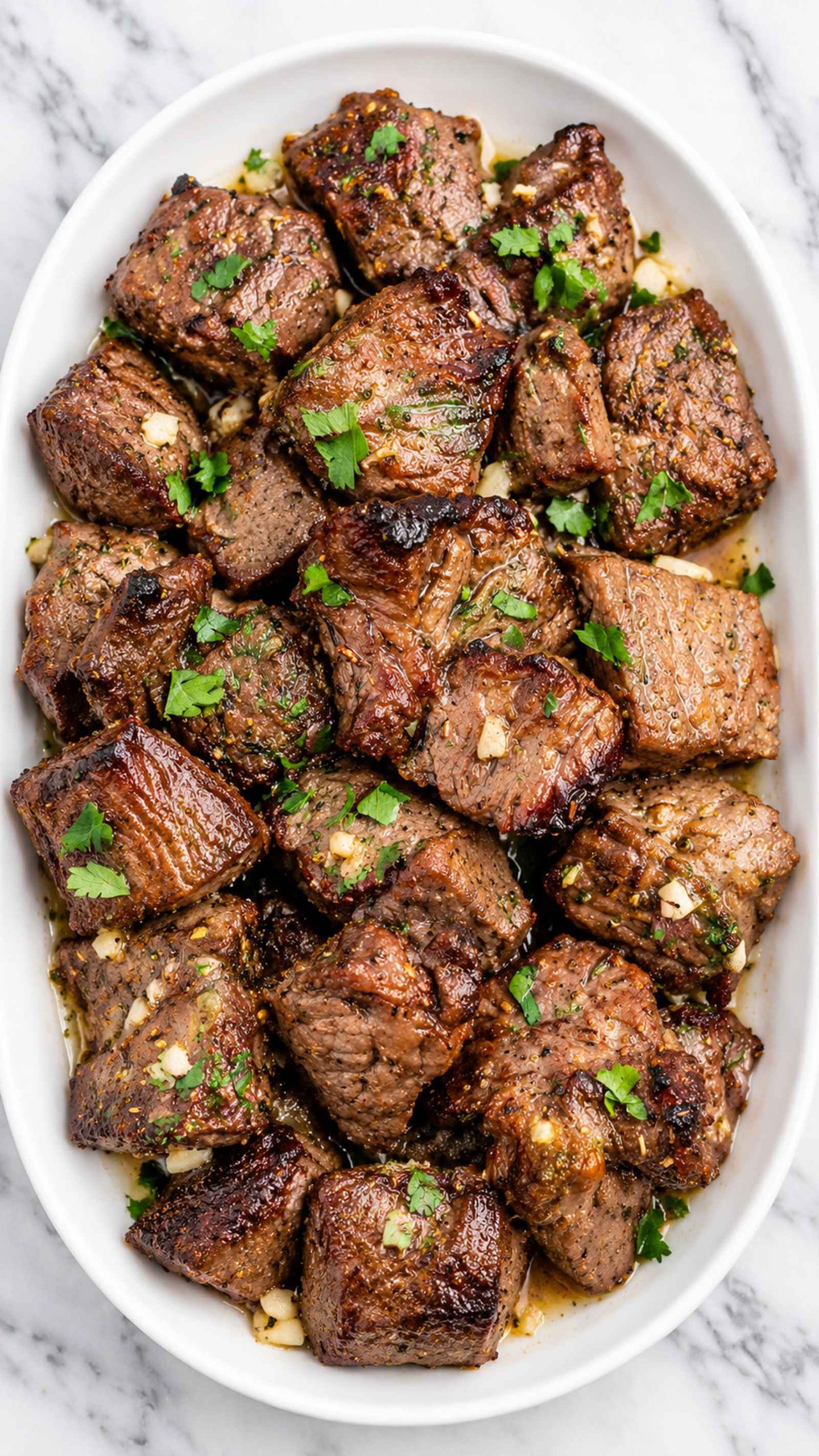 Delicious air fryer steak bites garnished with fresh herbs on a white platter.
